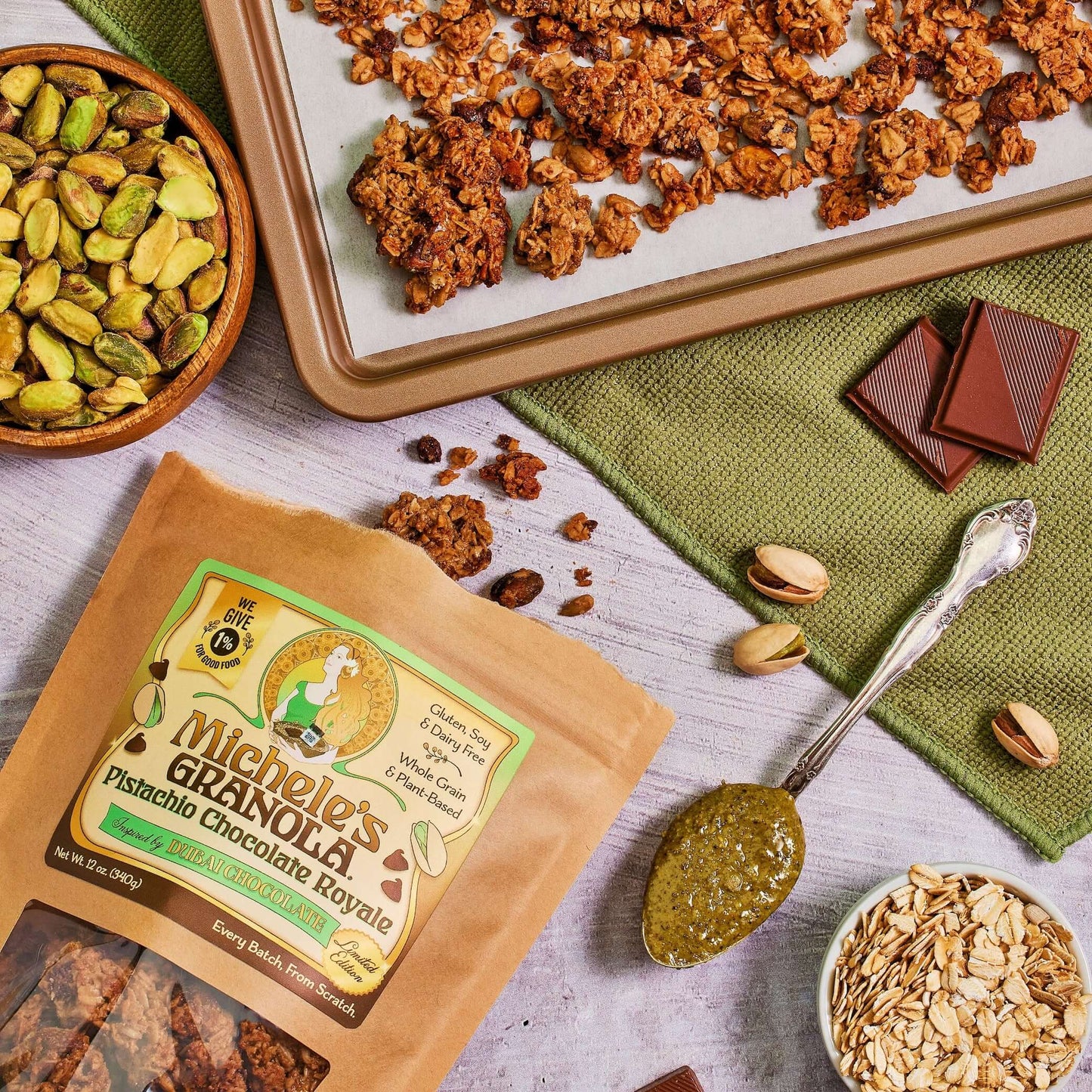 Michele's Pistachio Chocolate Royale Granola 12oz bag with sheet pan of granola and bowls of ingredients including pistachios, oats, and chocolate