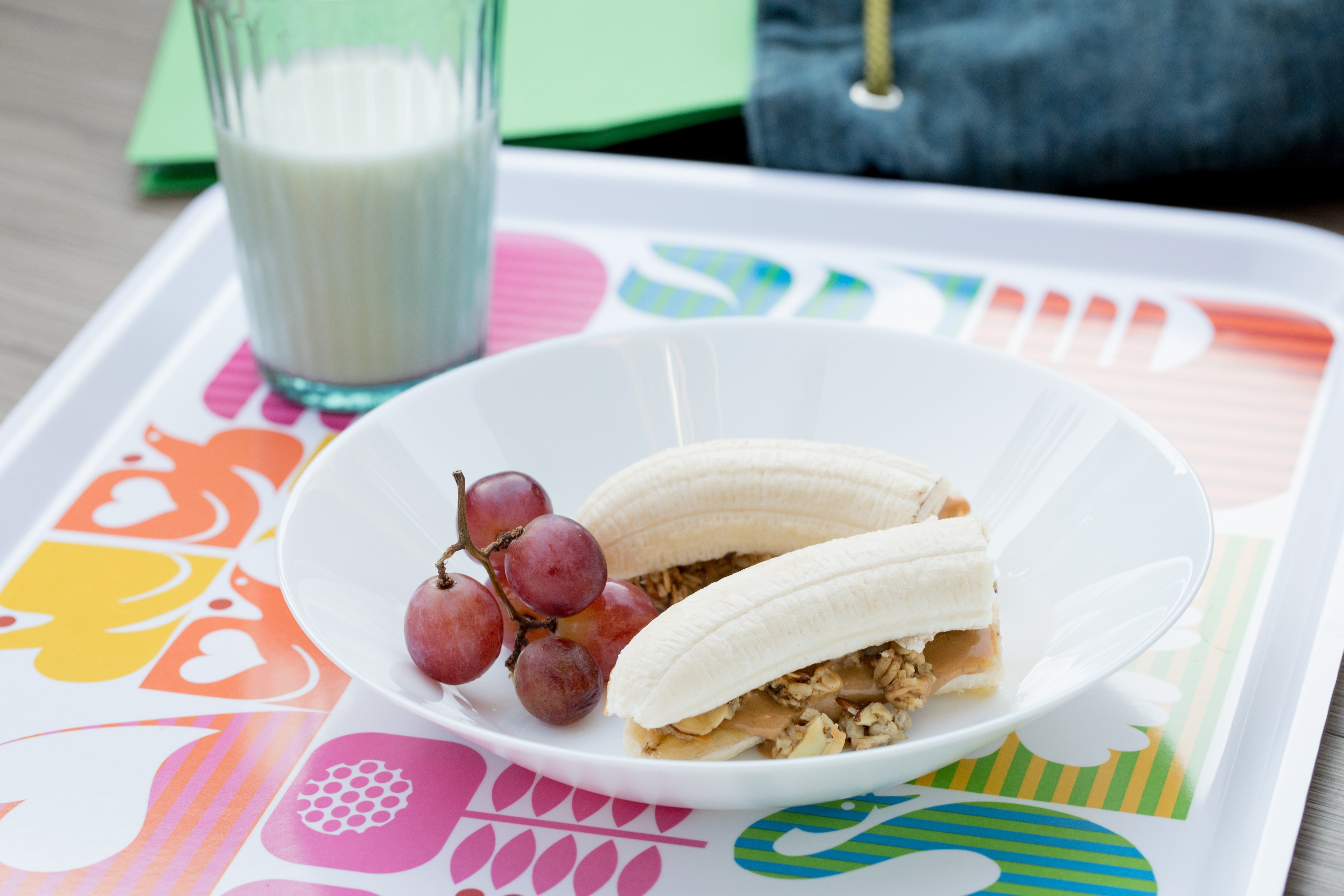 Banana with nut butter and Michele's Granola served with grapes and a glass of milk.