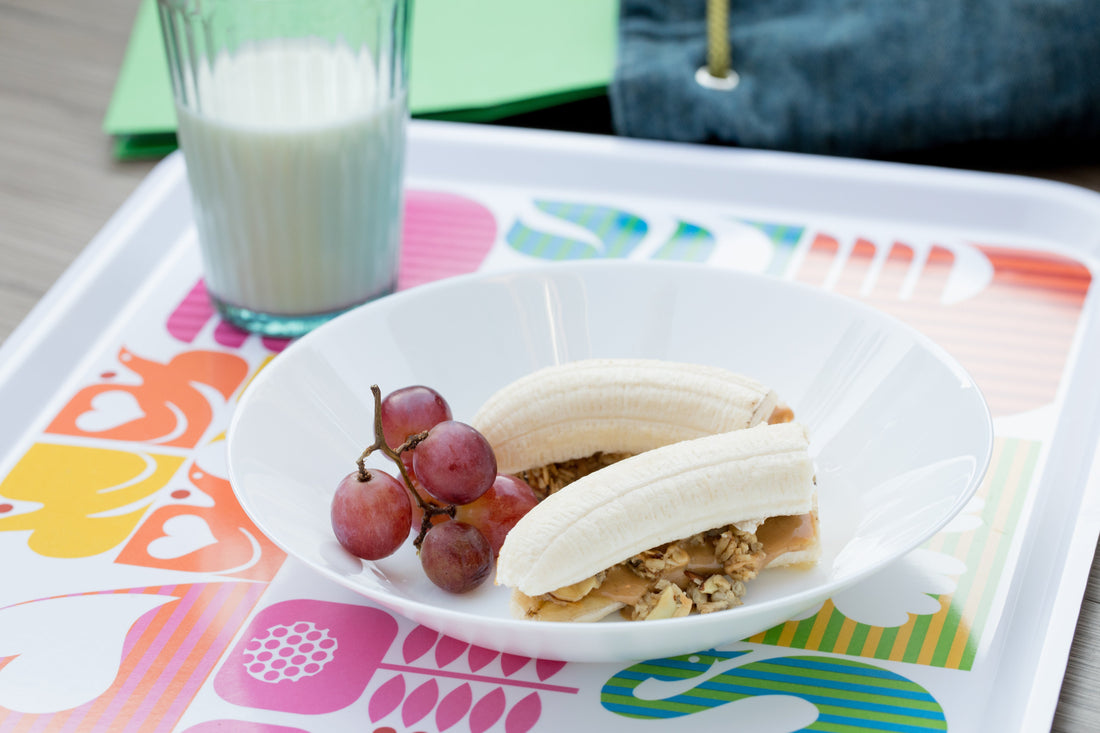 Banana with nut butter and Michele's Granola served with grapes and a glass of milk.