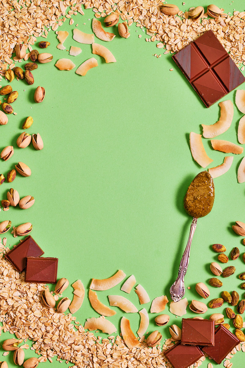 Michele's Granola chocolate pieces, nuts, and a spoon with a green background